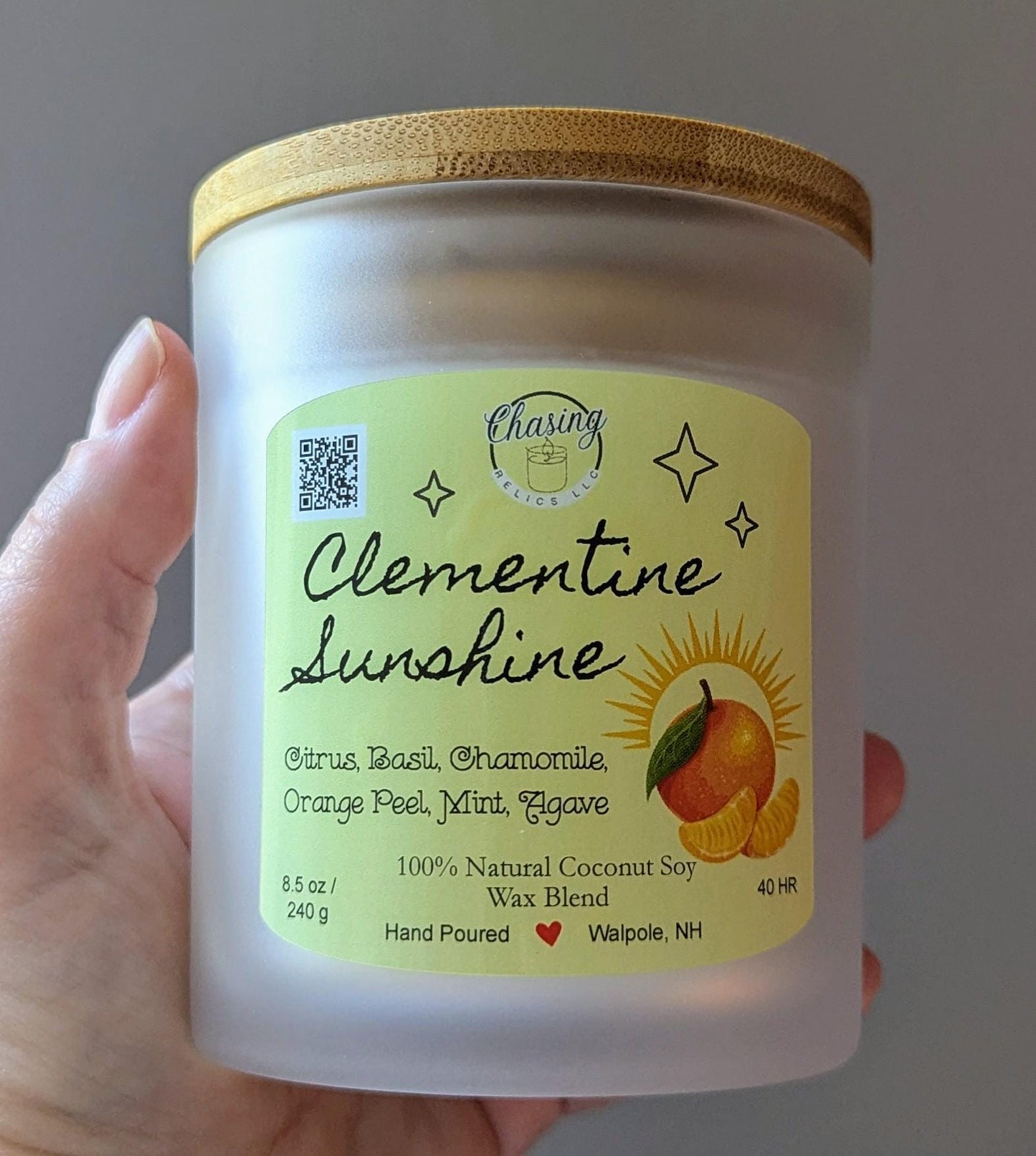 May include: A frosted glass candle jar with a bamboo lid. The label is yellow with black text and a graphic of a clementine. The text reads 'Chasing Relics LLC', 'Clementine Sunshine', 'Citrus, Basil, Chamomile, Orange Peel, Mint